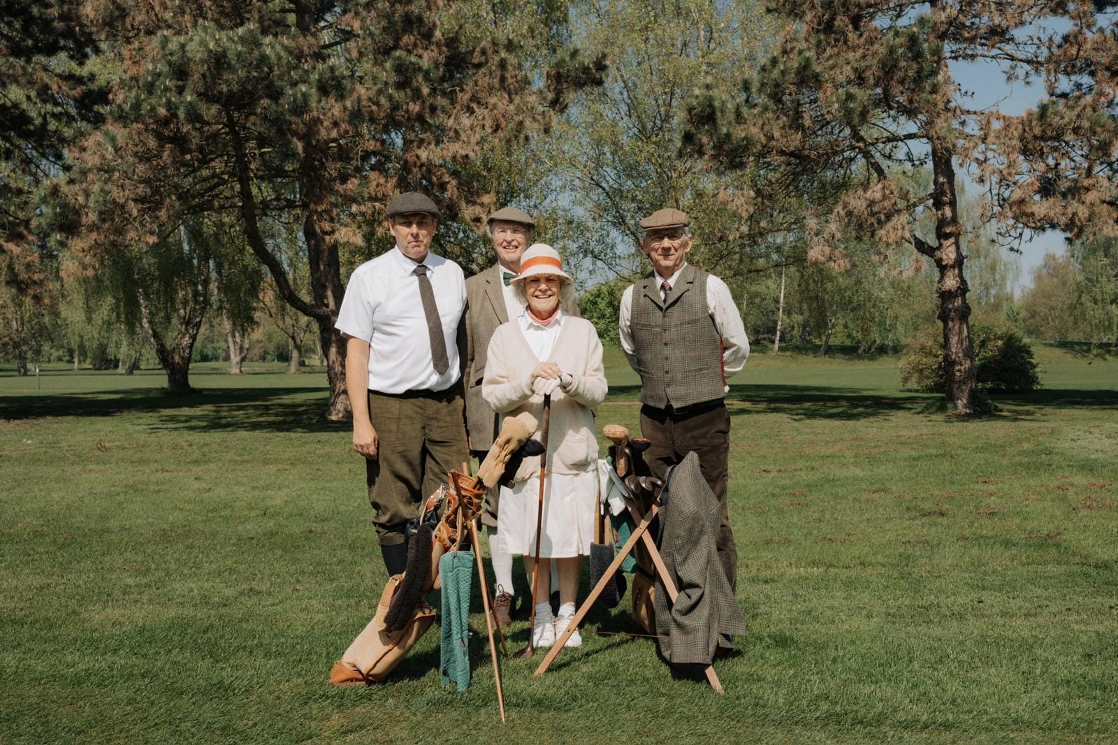 Vier ältere Menschen mit Golfausrüstung stehen auf einem Golfplatz zwischen Bäumen, lächeln und posieren für das Foto.