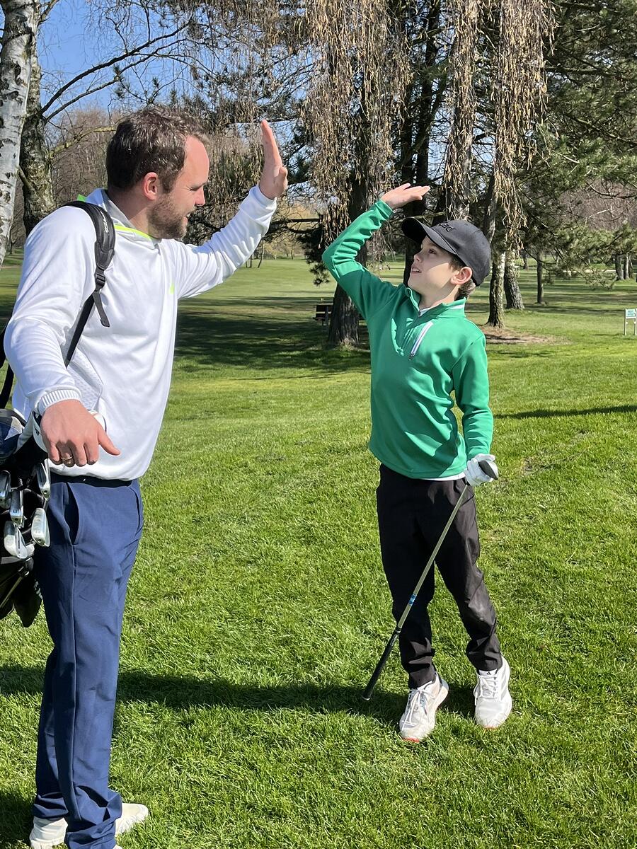 Ein Mann und ein Junge auf einem Golfplatz geben sich high five, während der Junge mit einem Golfschläger in der Hand steht.