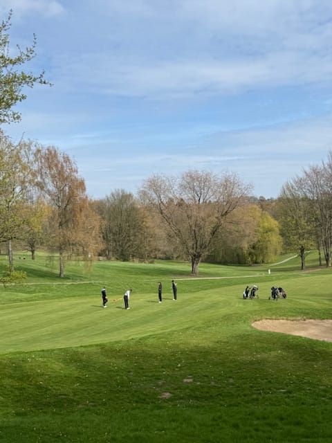 Menschen spielen Golf auf einem grünen Golfplatz an einem sonnigen Tag.