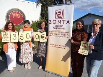Vier Frauen stehen neben einem Zonta-Stand mit einem Banner und halten eine Spendenscheck in Höhe von 350 Euro.