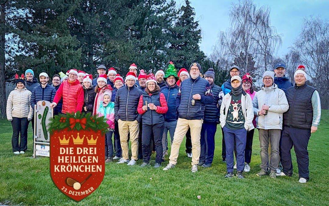 Eine Gruppe von Menschen, die festliche Kleidung und Weihnachtsmützen trägt, versammelt sich im Freien auf einer Wiese, um ein Weihnachtsfest zu feiern.